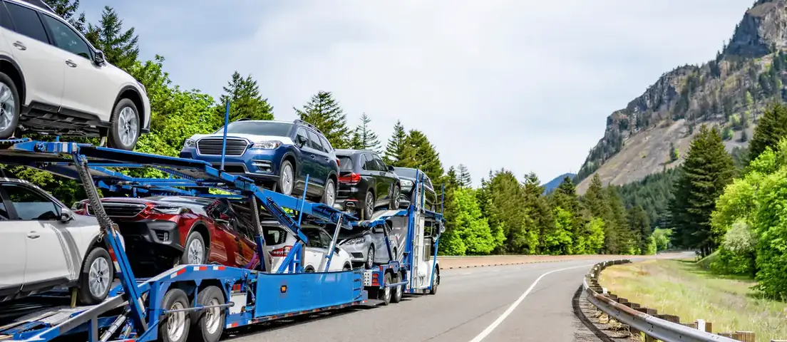 An open car carrier loaded with SUVs and sedans on a mountain highway